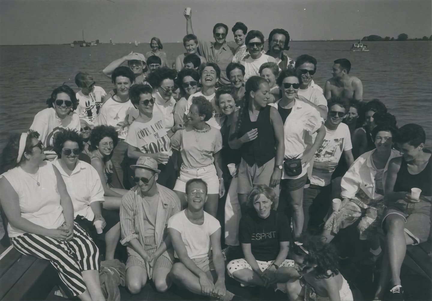 A large group of friends laughs together on a boat deck.